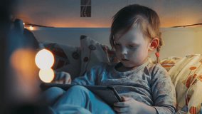 Little girl enjoys a tablet lying down in her bed before going to bed