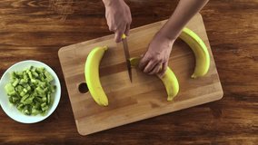 Hands peeling banana on wooden board, top view video