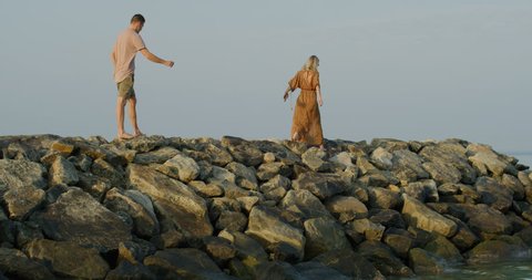 Young Beautiful Couple Walking on the Pier/ Dock Made of Rocks. Scenic View of Calm Sea and Sky. Shot on RED Epic 4K UHD Camera.