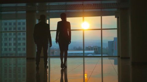 The man and woman walking in the office hall on a sunset background. slow motion