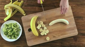 Woman hands slicing a banana for fruit salad, top view video