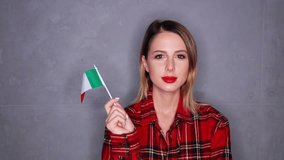Young redhead woman waving flag of Italy on grey background