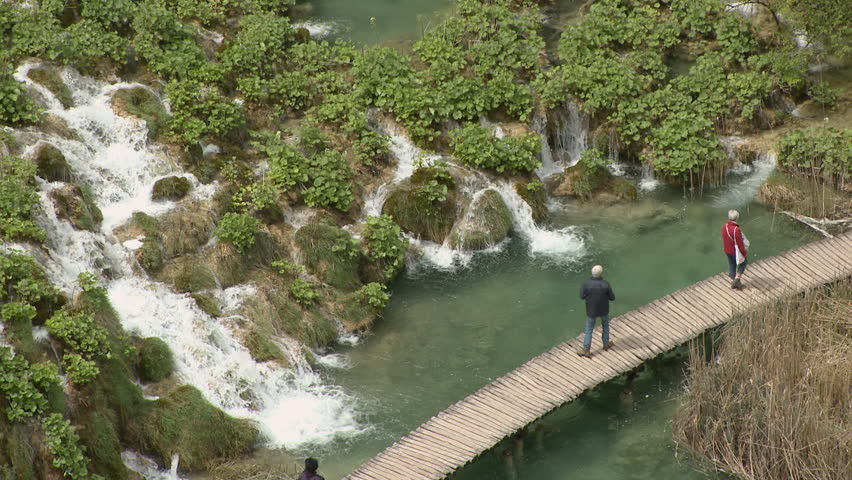 Plitvice Lakes, National Park,  Dinaric Alps, Croatia, a UNESCO World Heritage Site, tourists on walkways walking by water cascades running between plants growing on travertine dams, static shot