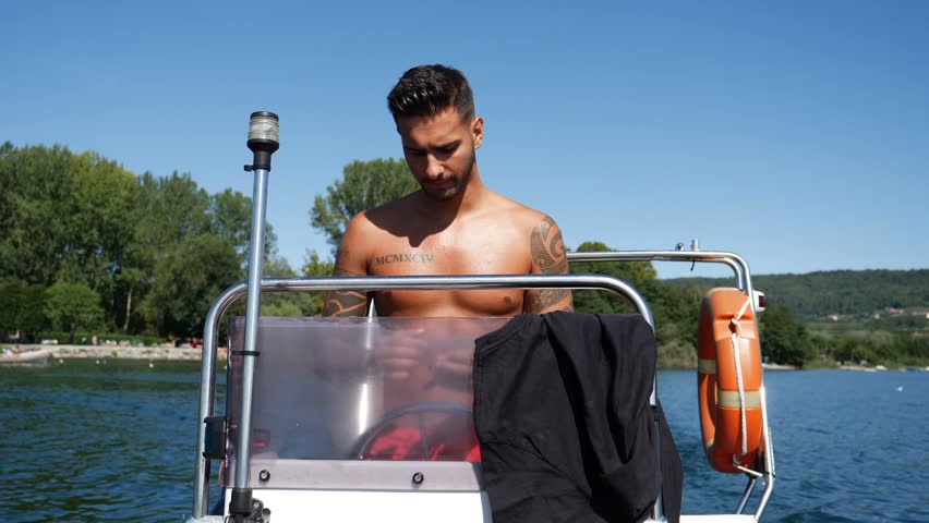 Portrait of young bearded handsome man with tattooed body looking sexually at camera sailing in boat.