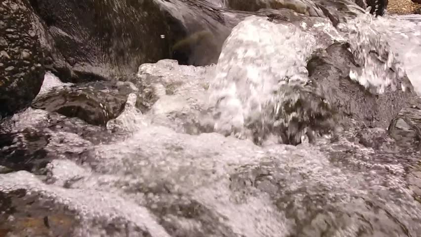 Small stream water pours over rock slow motion