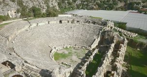 High angle aerial drone video of ancient Roman theater camera panning left to reveal rock-cut tombs at the Lycian League ruins of Myra in Demre, Turkey. 4k at 23.97fps