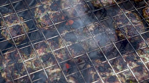 Very tight closeup of kofta cooking on a grill with smoke and flames.