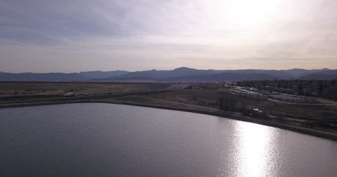 With the sun in our faces, we race along a body of water as we capture commuters along C470. The Hogback and local mountains pokes into the sky as the sun begins to set Video de stock