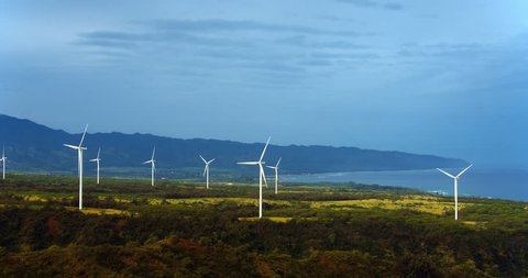 Aerial view of windmills spinning on sunny summer day in tropical forest environment 