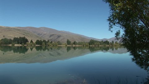 Wide shot on trees at the edge of Lake Waikati, Otago, reflecting in the water