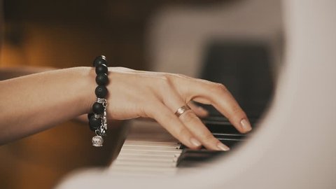 Female hands playing piano. Female hands with bracelet on piano. Woman touches fingers on keys. Close up.