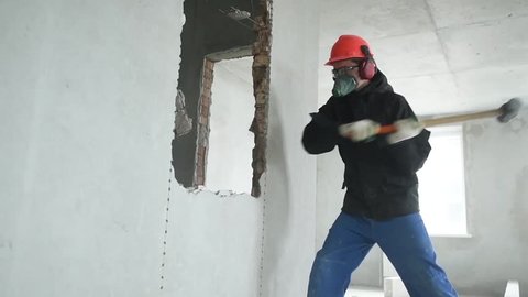 demolition work and rearrangement. worker with sledgehammer at wall destroying