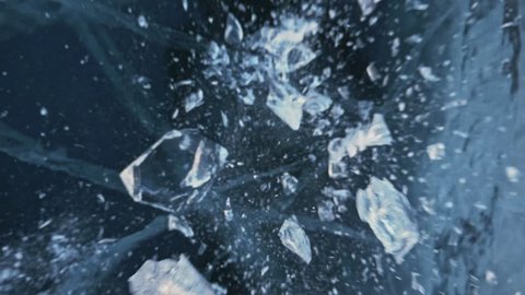 Man in the mittens smashes the ice on the ice. Slow motion. The camera moves behind the ice. A piece of ice is very beautifully broken about the icy with magical cracks. In the frame, a lot of
