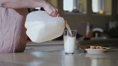 A glass of milk for breakfast. A woman pours milk from a 1-gallon plastic bottle into a glass