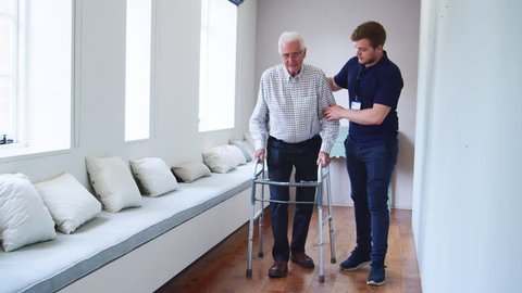 Male nurse helps senior man using walking frame, full length