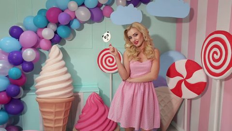 Portrait of a Barbie girl with blond curly hair in a pink dress and a big candy in her hands at a candy party.