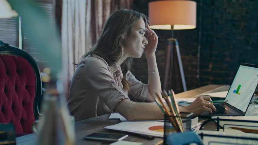 Exhausted business woman working on laptop computer in office. Businesswoman analyzing financial data on notebook at evening. Market researcher in office. Female worker in home office