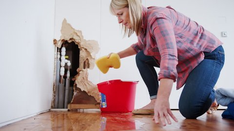 Mature Woman At Home Mopping Up Water From Leaking Pipe