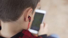 Little boy playing a videogame and listen to music with a smartphone wearing red headphones.