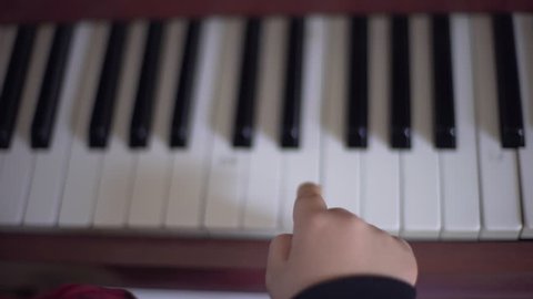 Overhead POV shot of little boy learning to play piano and playing it with one finger. Learning music. School of music.