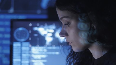 portrait of young woman programmer working at a computer in the data center filled with display screens