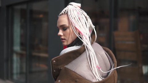 girl with an unusual appearance on the background of urban architecture. teenager with dreadlocks and piercing. a modern youth culture. back view. slow motion