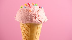 Ice cream cone close-up. Icecream scoop in waffle cone design rotated over pink color background. Strawberry or raspberry flavor Sweet dessert closeup, rotation. 4K UHD video