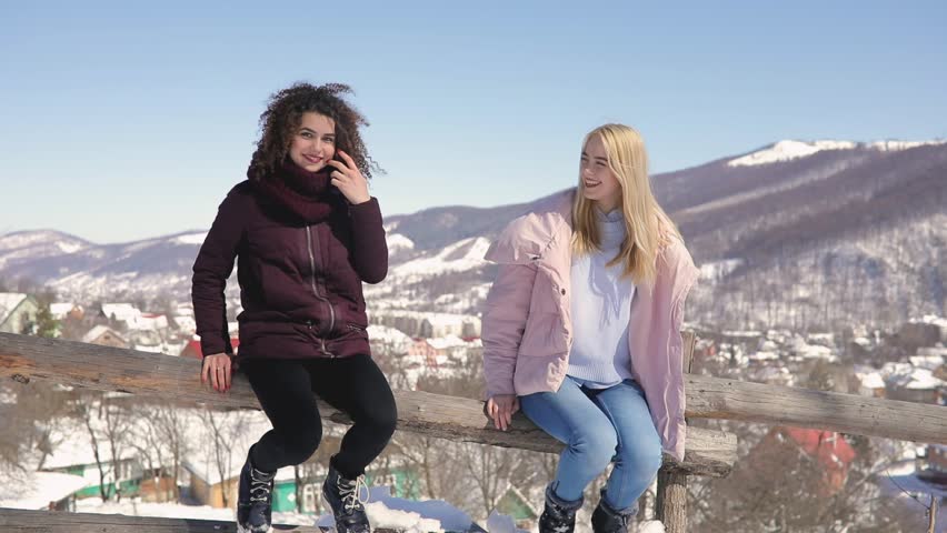 Women friends having fun, they jumping from fence to snowy ground