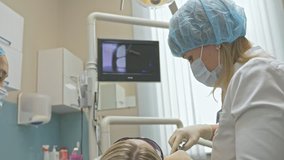 Doctor used special Dental Intraoral Check Digital Micro Camera to exam teeth. On the monitor dentist and patient see video of teeth, tooth problems. Doctor and assistant work in protective masks
