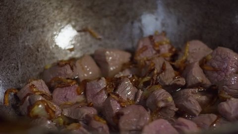 Close up shot of cast iron frying pan with meat cubes and chopped onions inside, cook shaking it
