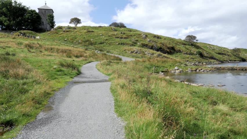 POV shot. Group of tourists enjoy historical monument on Norwegian fjord. Movement of someone, something along amazing landscape. Hilly terrain is covered with green thick grass, great waterfront