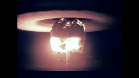 CIRCA 1954 - A nuclear device is detonated from a firing barge and the resulting mushroom cloud is shown at Bikini Atoll.