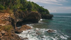 A picturesque landscape of Nusa Dua Bali coastline seashore with rocks, bright vegetation and azure ocean waves at bright sunny day. 4k video.