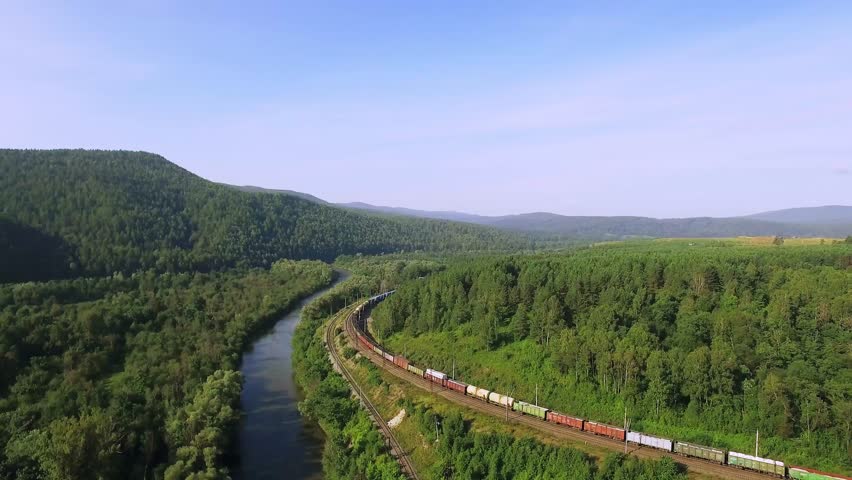 Freight train carries an electric locomotive by two-sided Trans Siberian railway near river in the Ural Mountains - Aerial Photography, top view Royalty-Free Stock Footage #1009432073