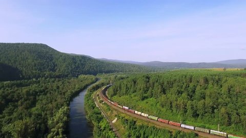 Freight train carries an electric locomotive by two-sided Trans Siberian railway near river in the Ural Mountains - Aerial Photography, top view