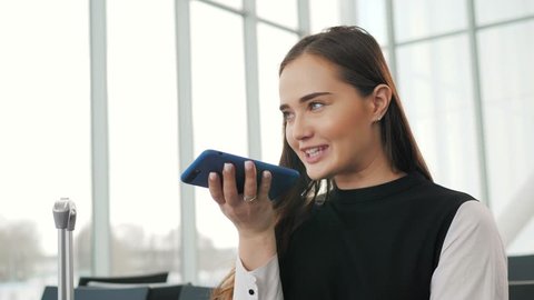 Portrait of a girl using the voice recognition of the phone and looking at cell phone near airport terminal in hotel on vacation tourist speech personal assistant natural language user interface