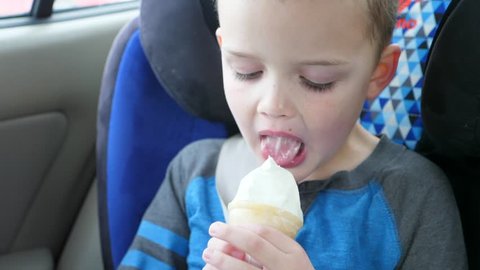 A slow motion shot of a cute young boy eating a vanilla ice cream cone in his car seat while driving