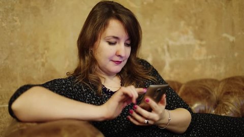 Woman sits on couch and uses smart phone near frayed wall