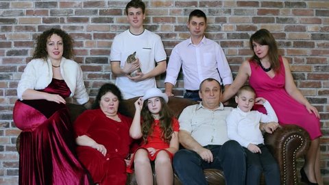 Eight members family poses around couch near brick wall