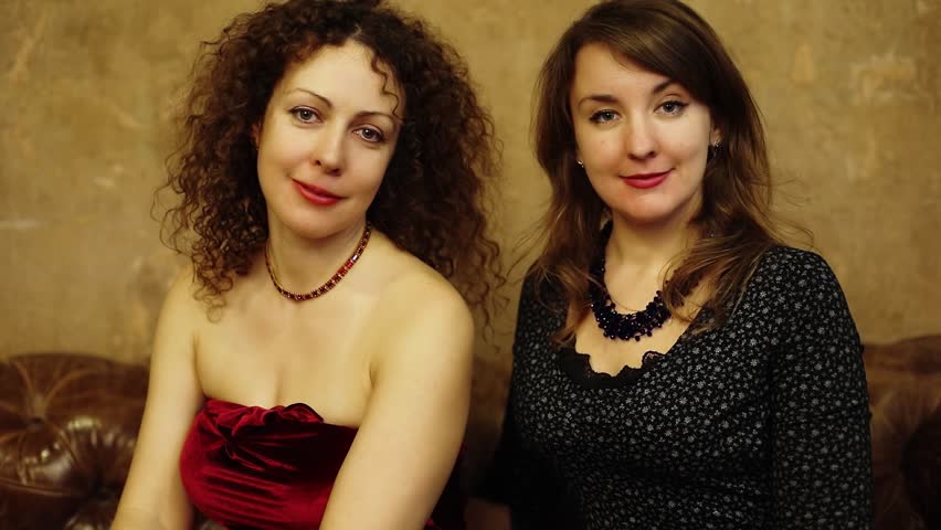 Two women sit on couch and look on each other near frayed wall