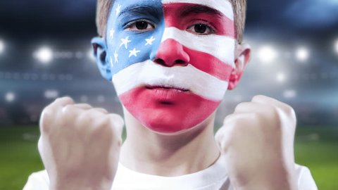 Kid with this his face painted withe the American flag and stadium as background: stockvideo