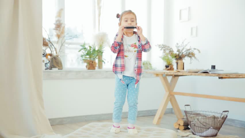 Pretty little girl playing harmonica in big bright room
