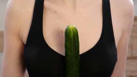 Closeup woman's hands dress the condom on cucumber.