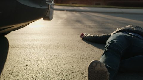 Man laying in street with cell phone near car bumper after accident / Cedar Hills, Utah, United States