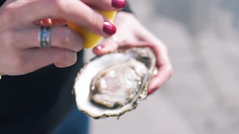 Close-up shot of women pouring lemon juice on the open oysters at the street. Delicious seafood in hand, Dynamic Slow motion