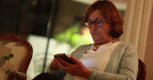 Casual real life candid 4K clip of 60 year old woman using cellphone device at night. Older woman using smartphone to communicate on the internet