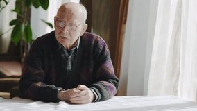 Serious senior man taking off glasses while sitting at table