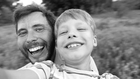 Portrait of happy caucasian family spinning around while taking selfie in countryside. Laughing daddy and son posing for camera in sunset time on summer day. Slow motion wide angle hd video footage.