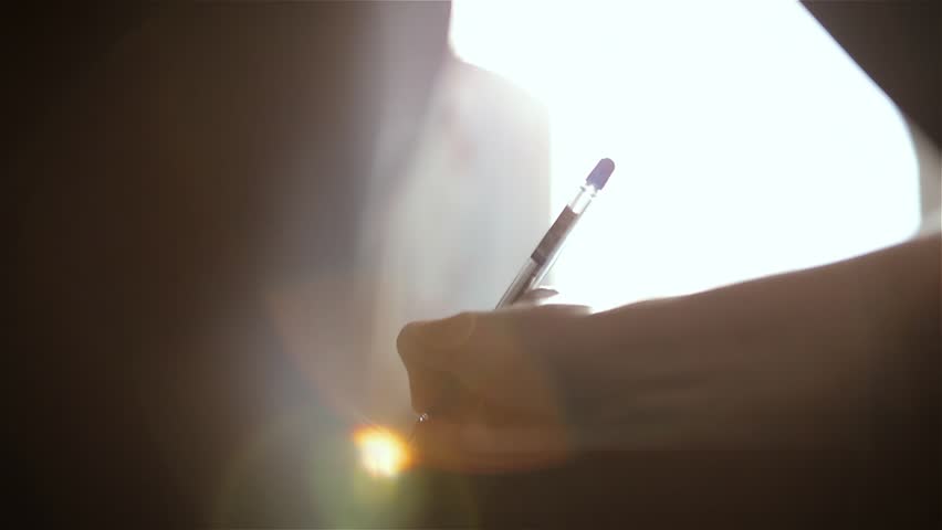 Close-up. A woman is writing a pen with a letter sitting at the table.