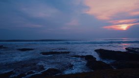 Amazing view colorful sunset on the ocean beach on Bali island, foaming waves, awesome purple pink and blue sky, rocks, video 4K with camera movement, wonderful nature